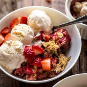 White bowl filled with baked fruit crisp and topped with ice cream and fresh fruits