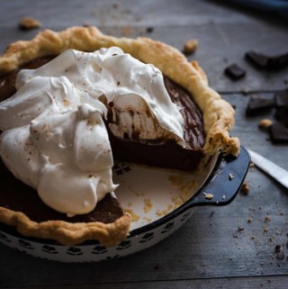 chocolate cream pie topped with meringue and a quarter missing sitting on a wooden table