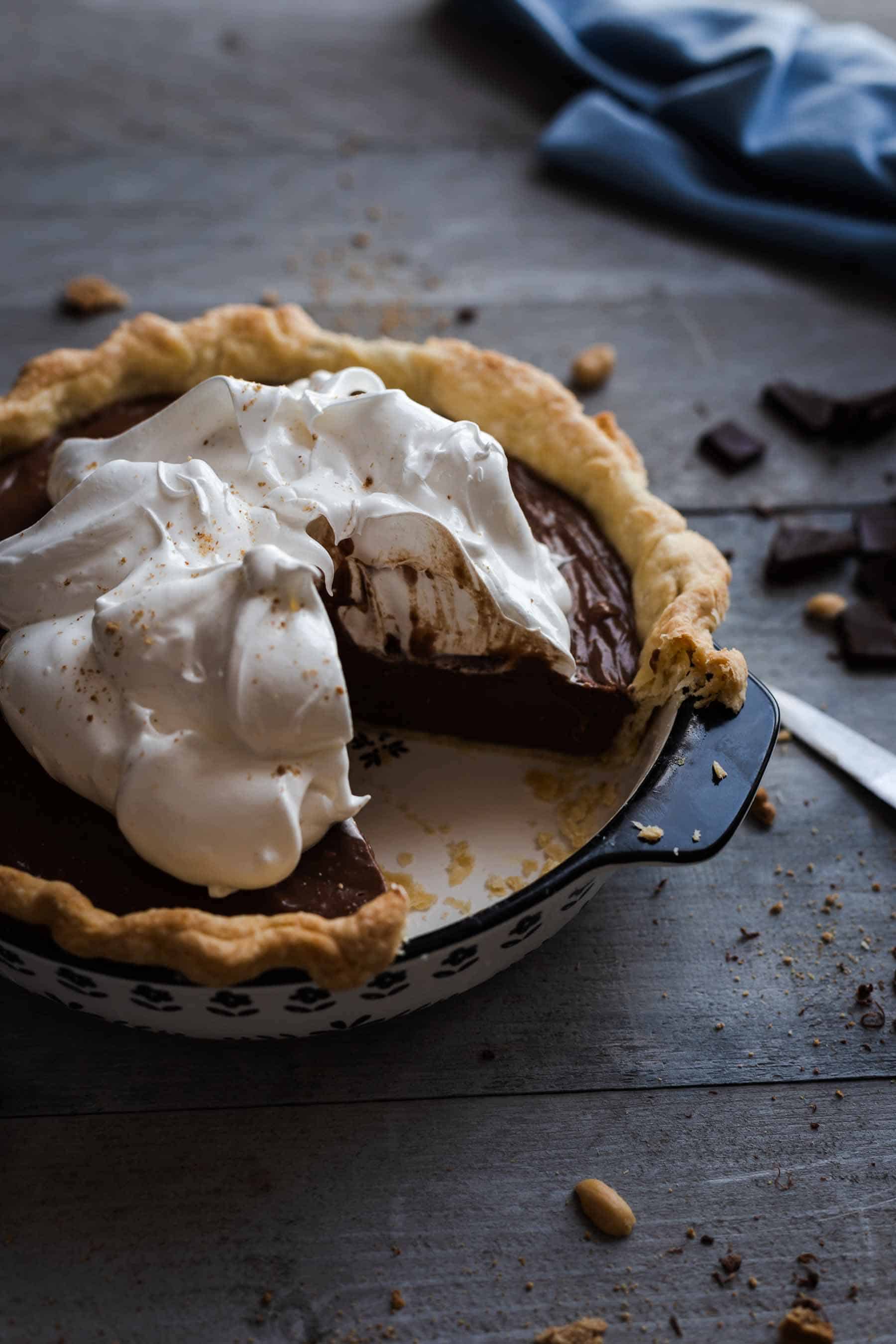 chocolate cream pie topped with meringue and a quarter missing sitting on a wooden table
