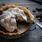 chocolate cream pie topped with meringue and a quarter missing sitting on a wooden table