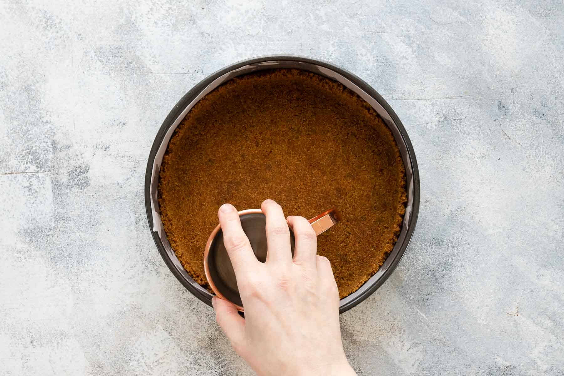 pressing down graham cracker crust into the bottom of a springform pan