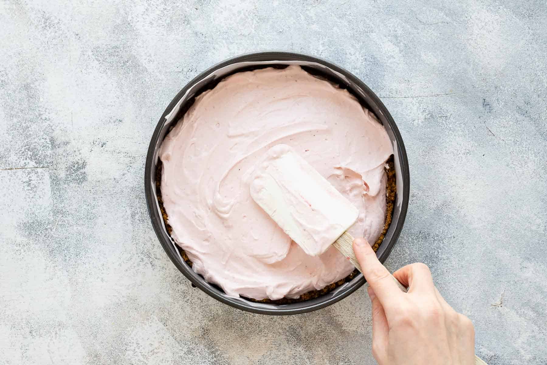 smoothing out cream cheese filling with a spatula in a springform pan