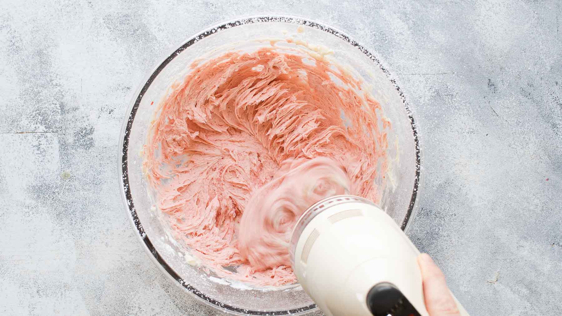 Mixing strawberry frosting in large mixing bowl