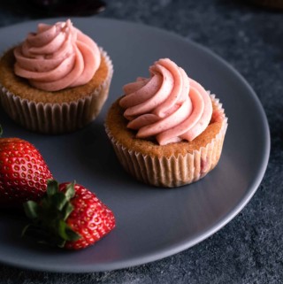 Two strawberry cupcakes on serving plate with fresh strawberries