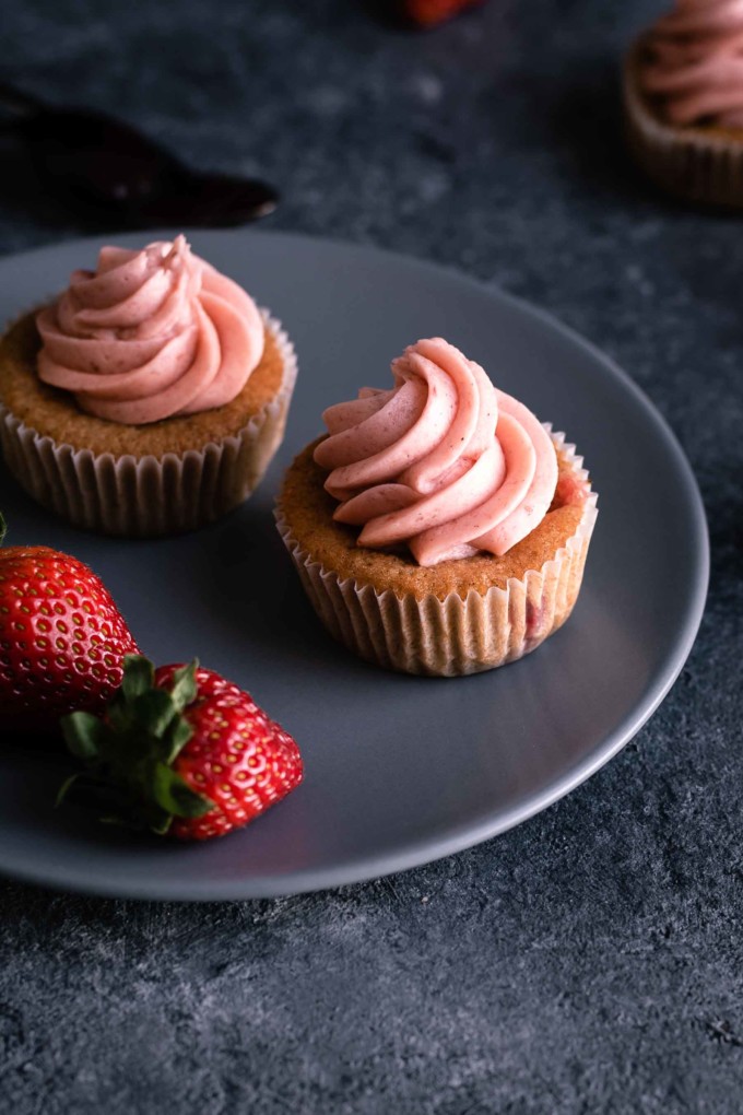 Two strawberry cupcakes on serving plate with fresh strawberries