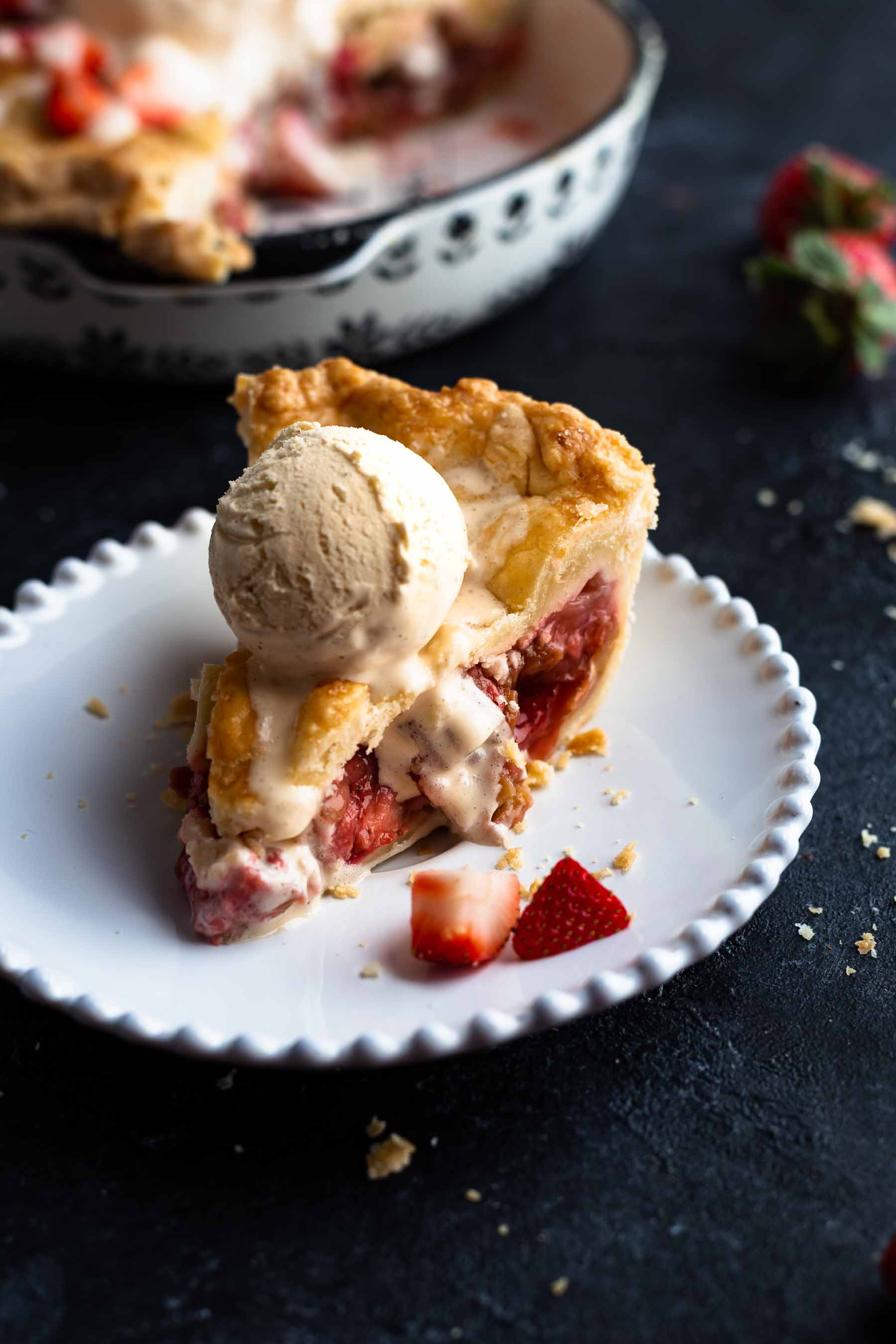 a slice of strawberry rhubarb pie on a serving plate with a scoop of ice cream on top
