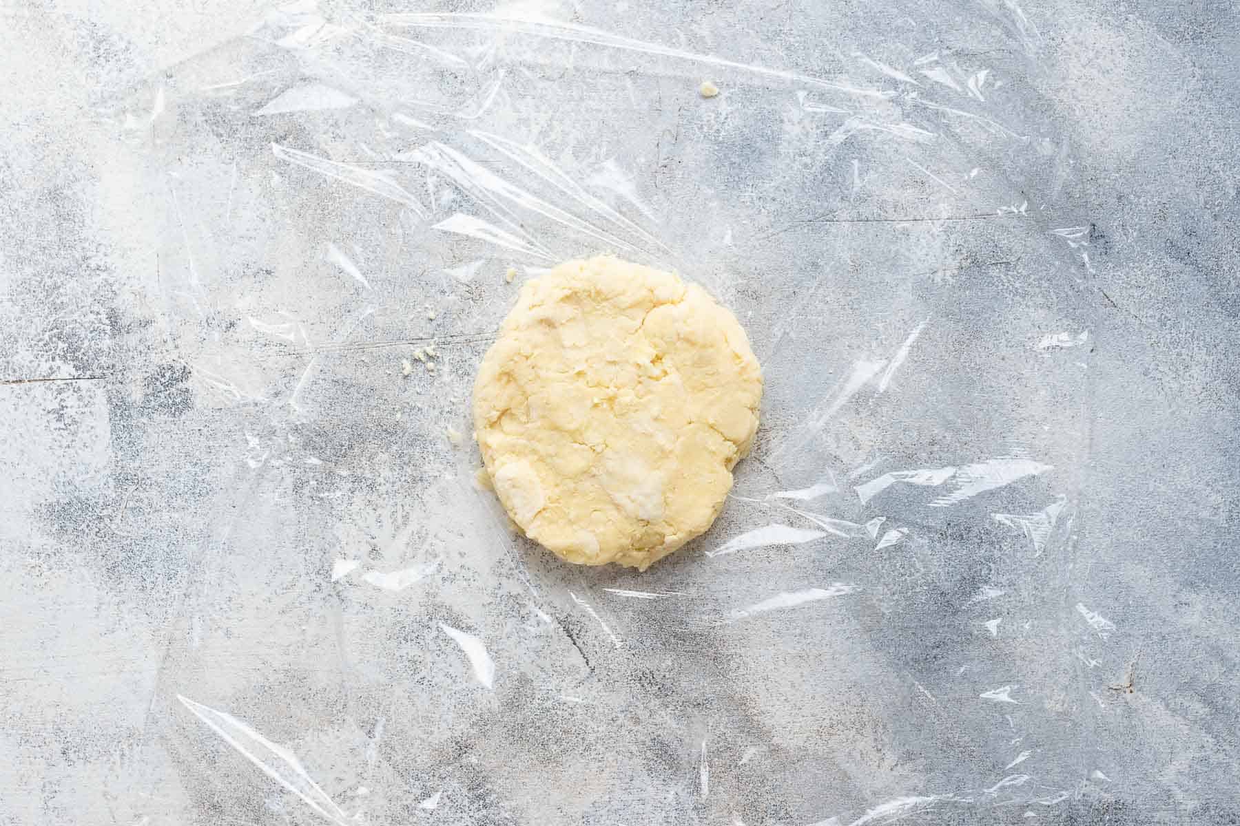 pie crust shaped into a disc sitting on a piece of plastic wrap