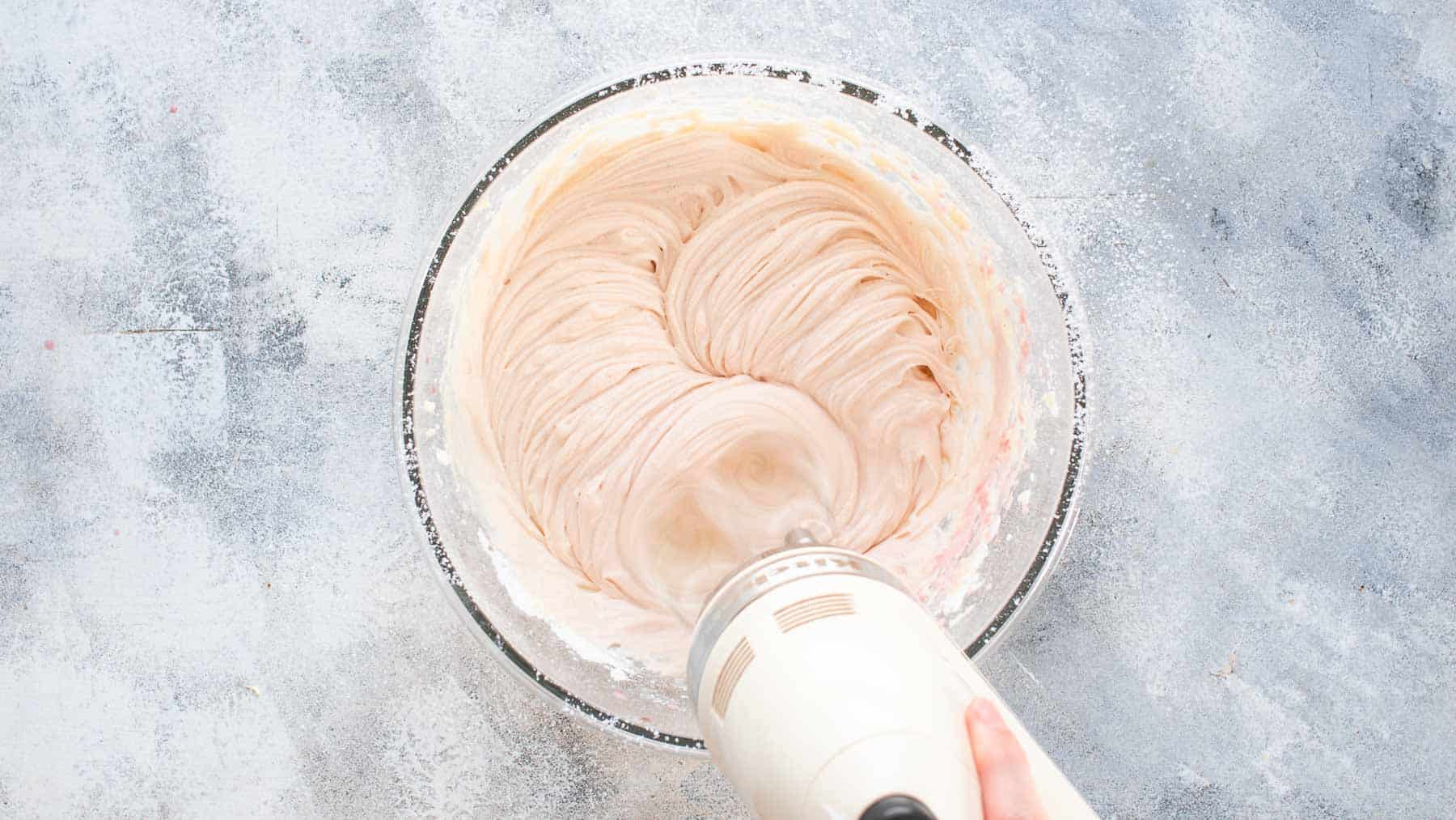 mixing cream cheese frosting in a glass bowl