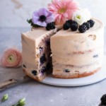 Blackberry cake with flower decoration on a serving plate that has a slice taken out