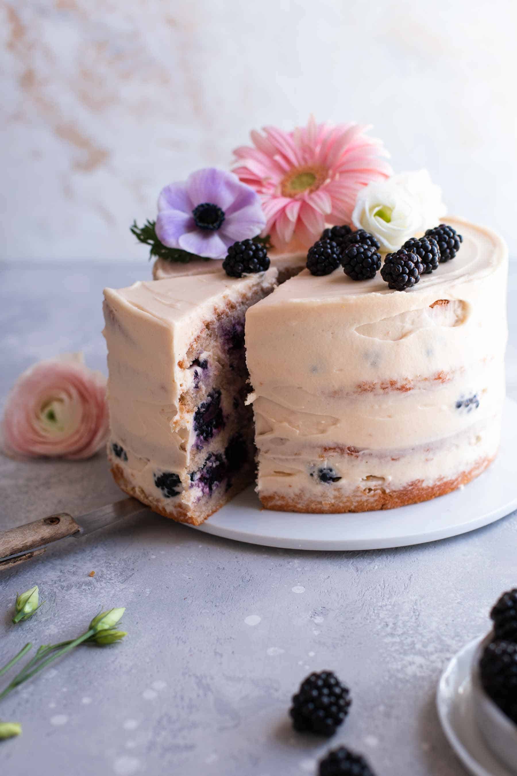 Blackberry cake with flower decoration on a serving plate that has a slice taken out