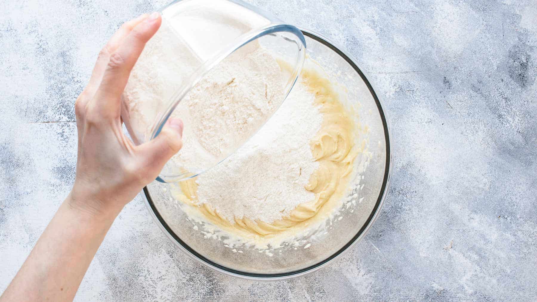 adding flour to cake batter in a bowl