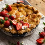 rhubarb pie with strawberries on top sitting on wooden table