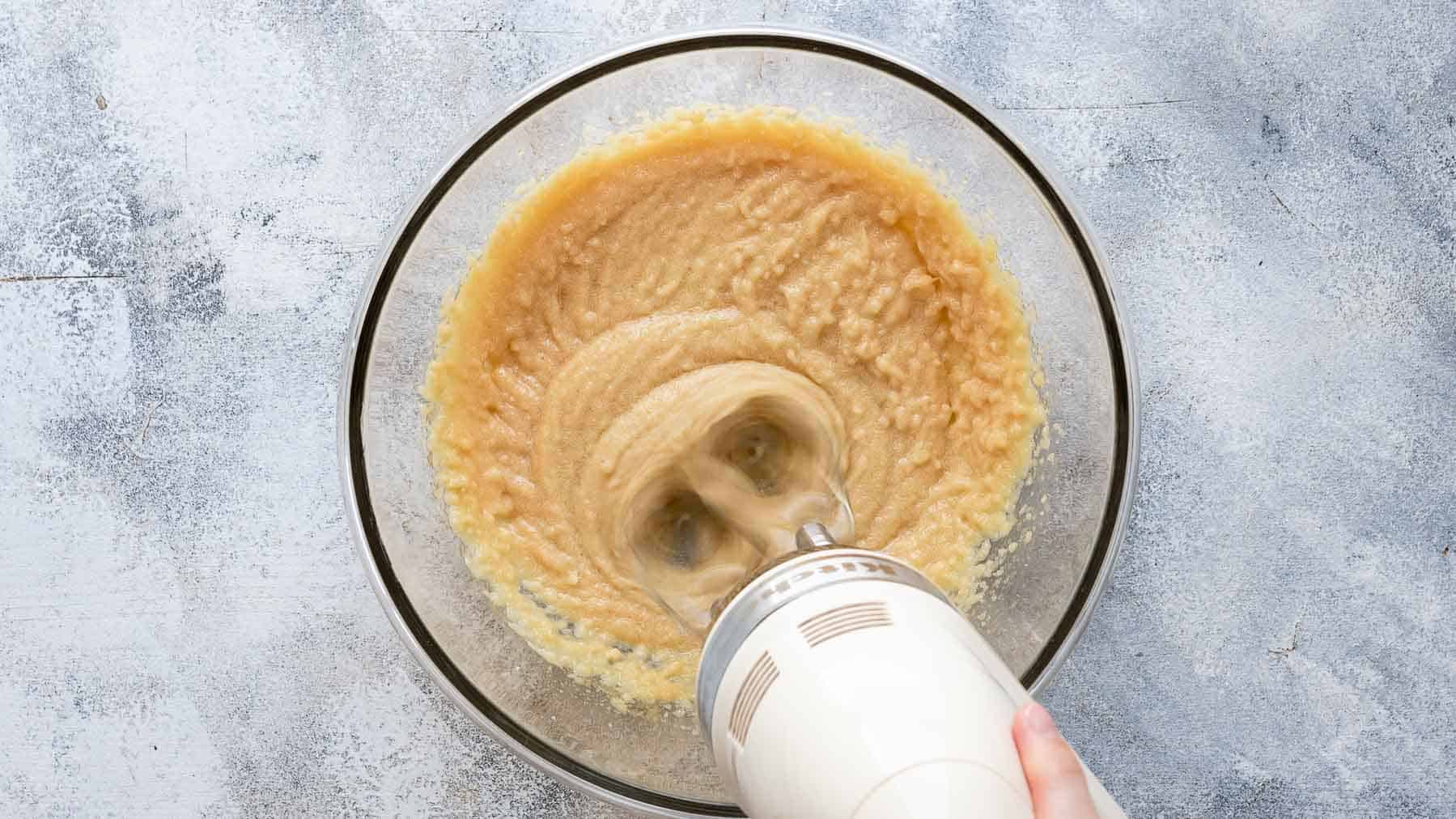 mixing butter, oil, and sugar with an electric mixer in a bowl