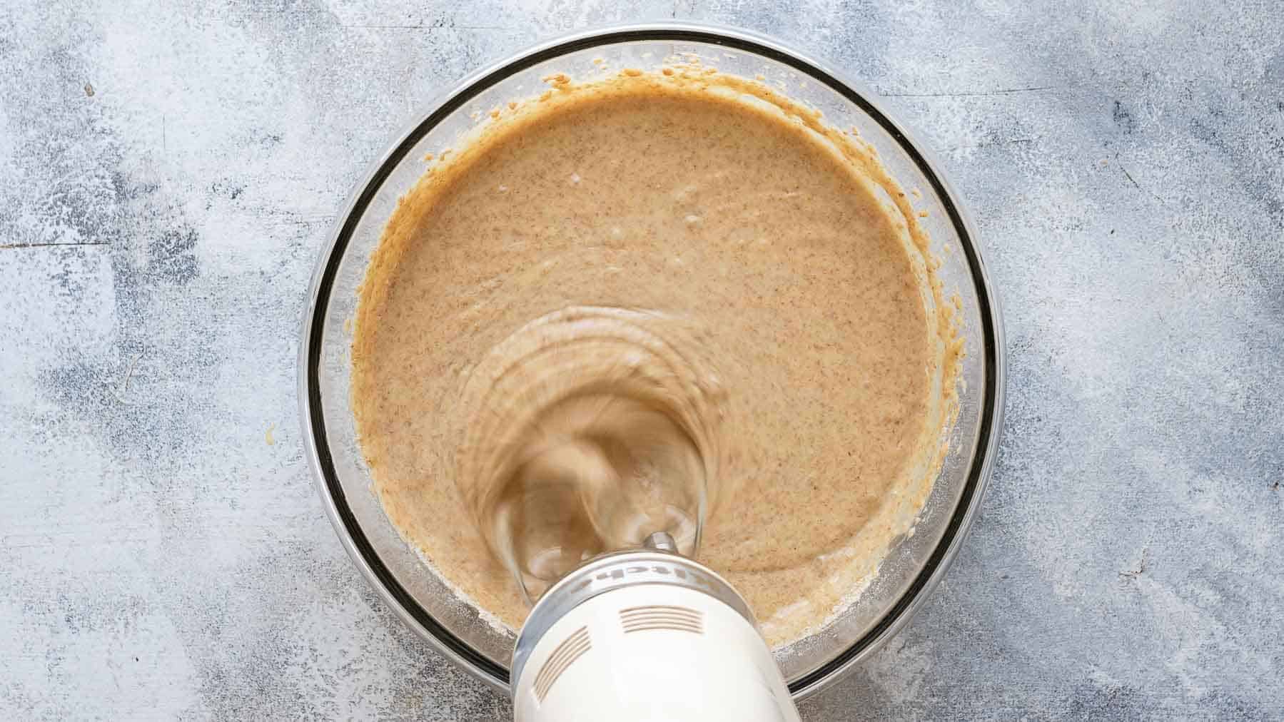 mixing graham cracker cake batter with an electric mixer in a bowl