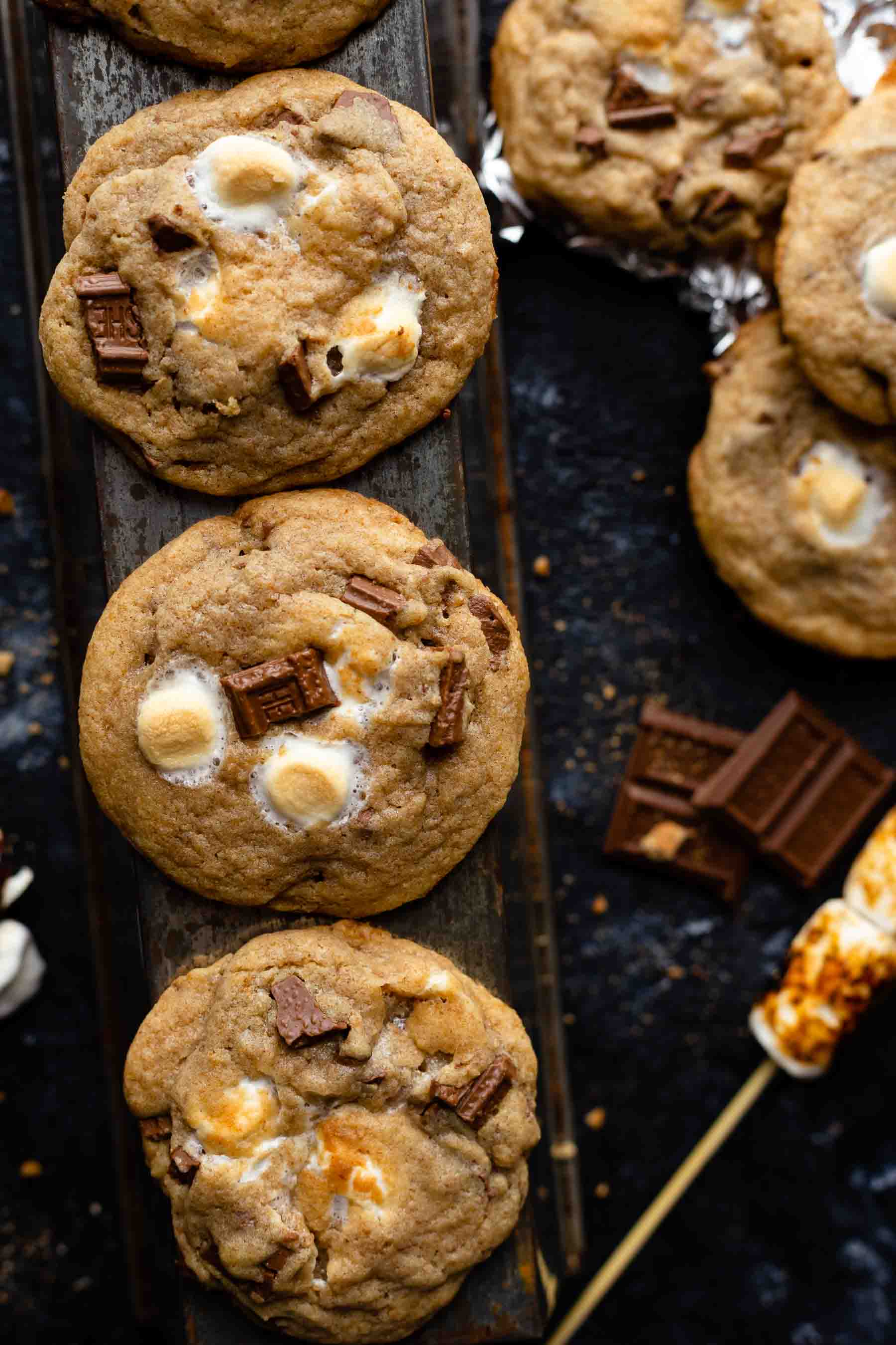 a half dozen baked cookies filled with chocolate pieces and marshmallows on a dark table