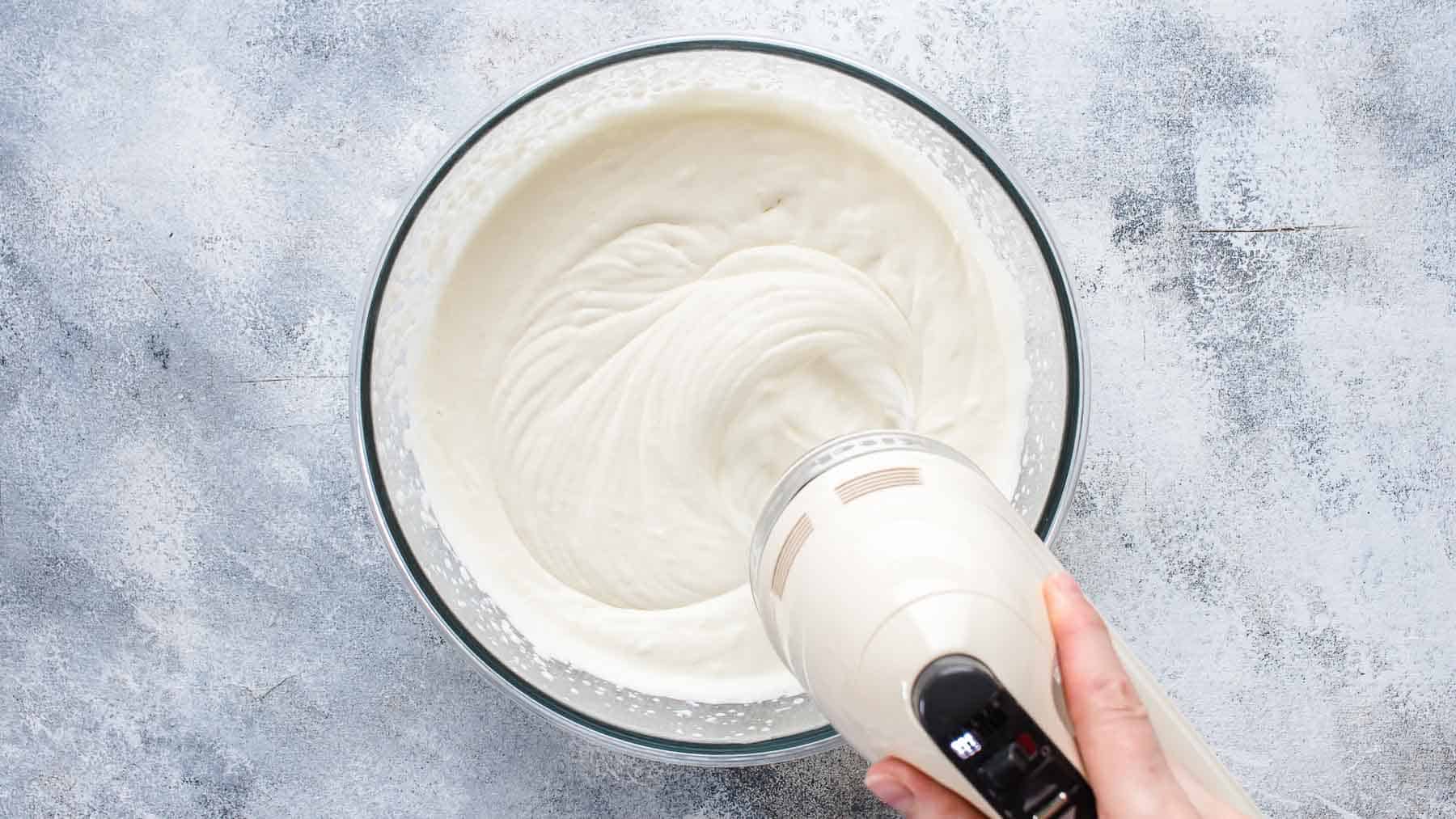 whipping cream with an electric mixer in a mixing bowl