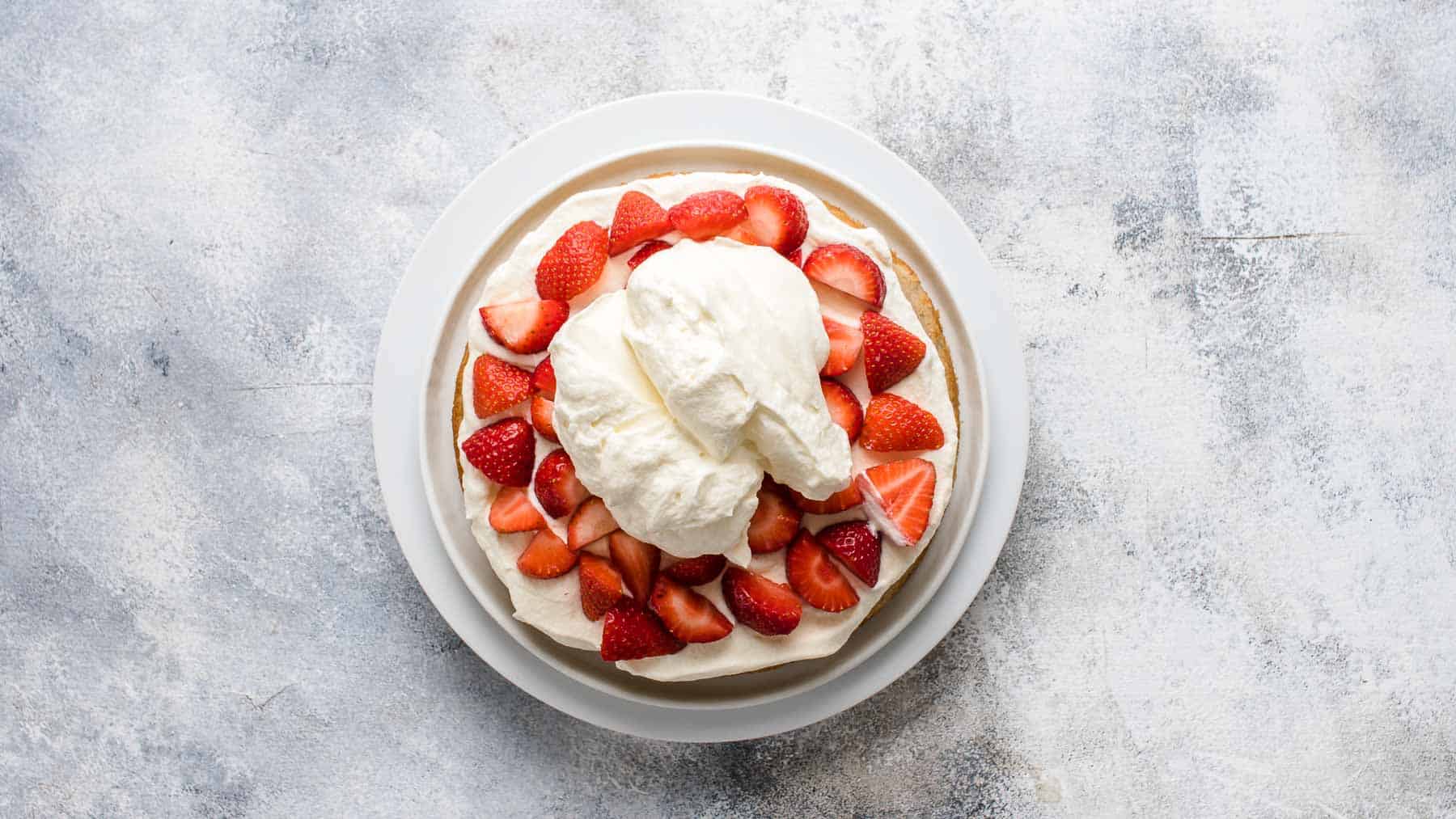 cake layer topped with whipped cream and fresh strawberries on a cake turner