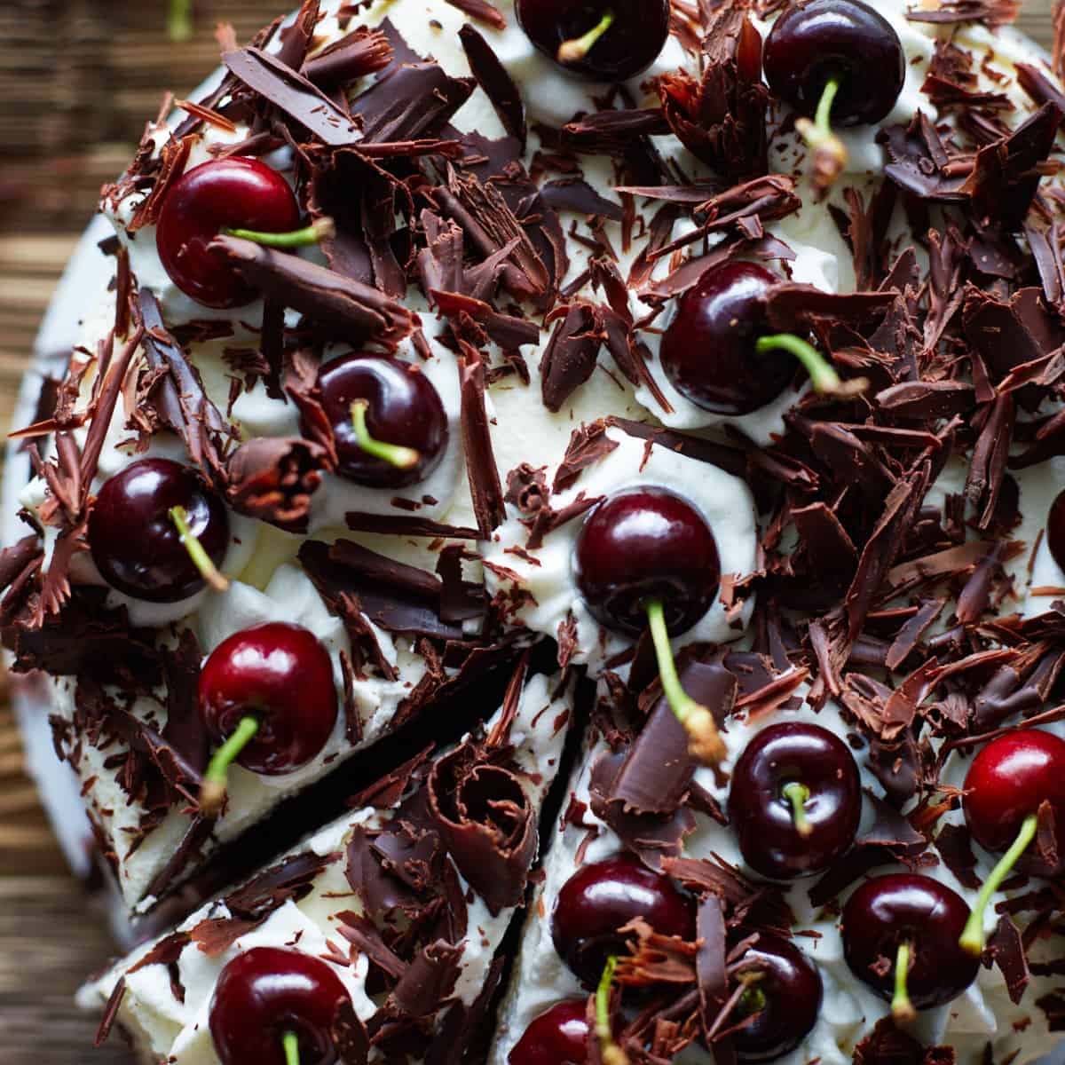 Close up of decroated cake covered in whipped cream, chocolate curls and cherries