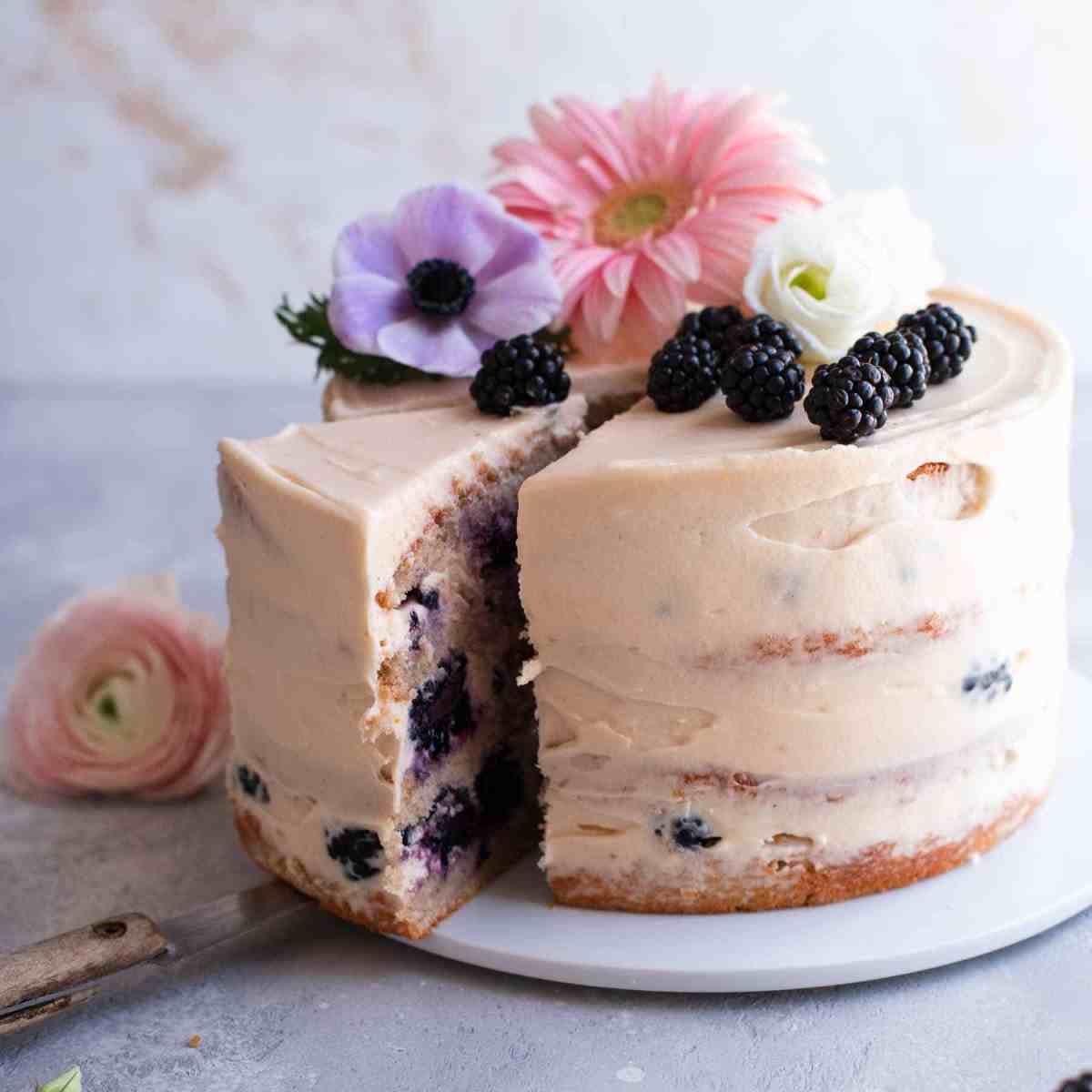 Blackberry cake with flower decoration on a serving plate that has a slice taken out
