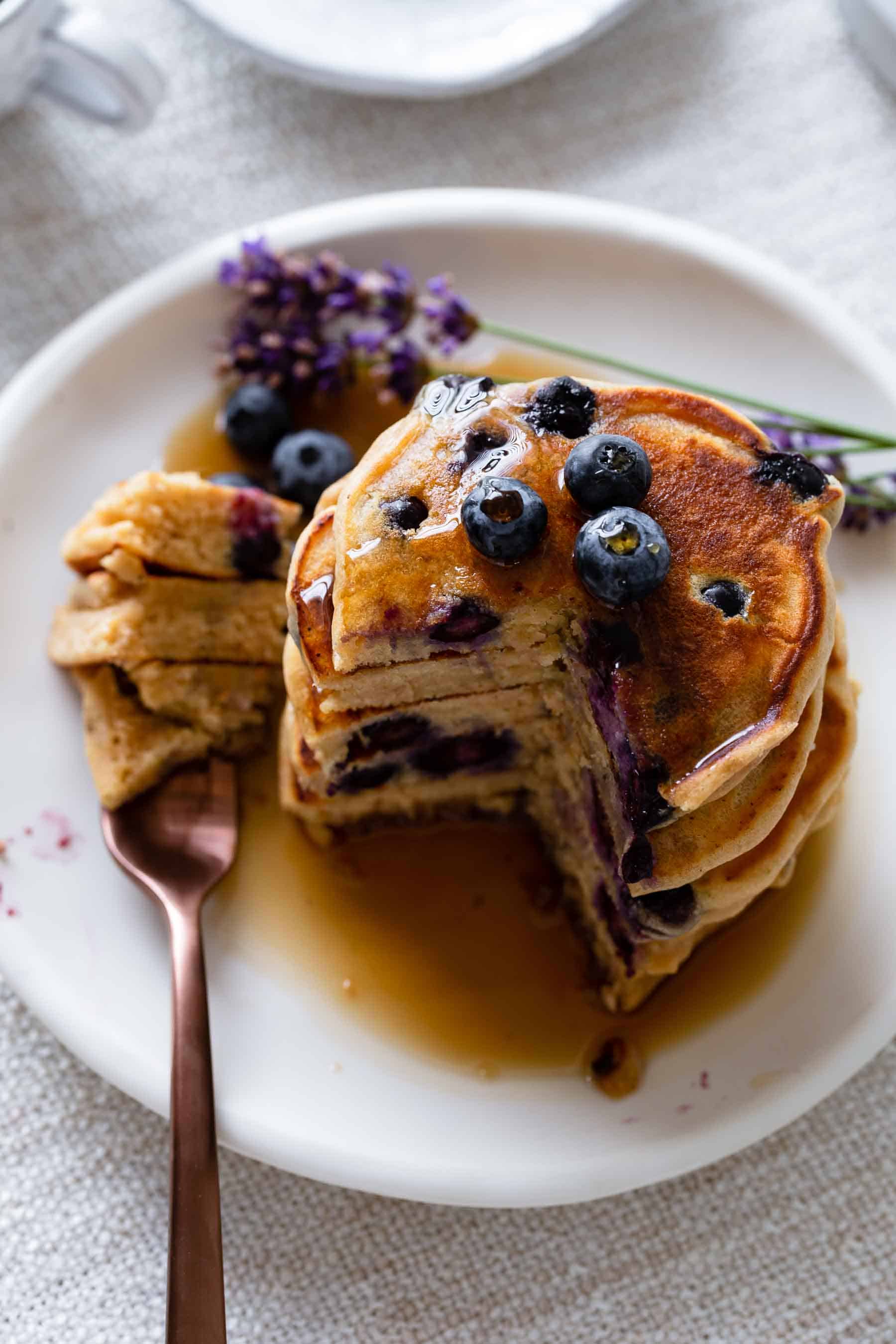 a stack of blueberry pancakes on a white plate with a fork and syrup