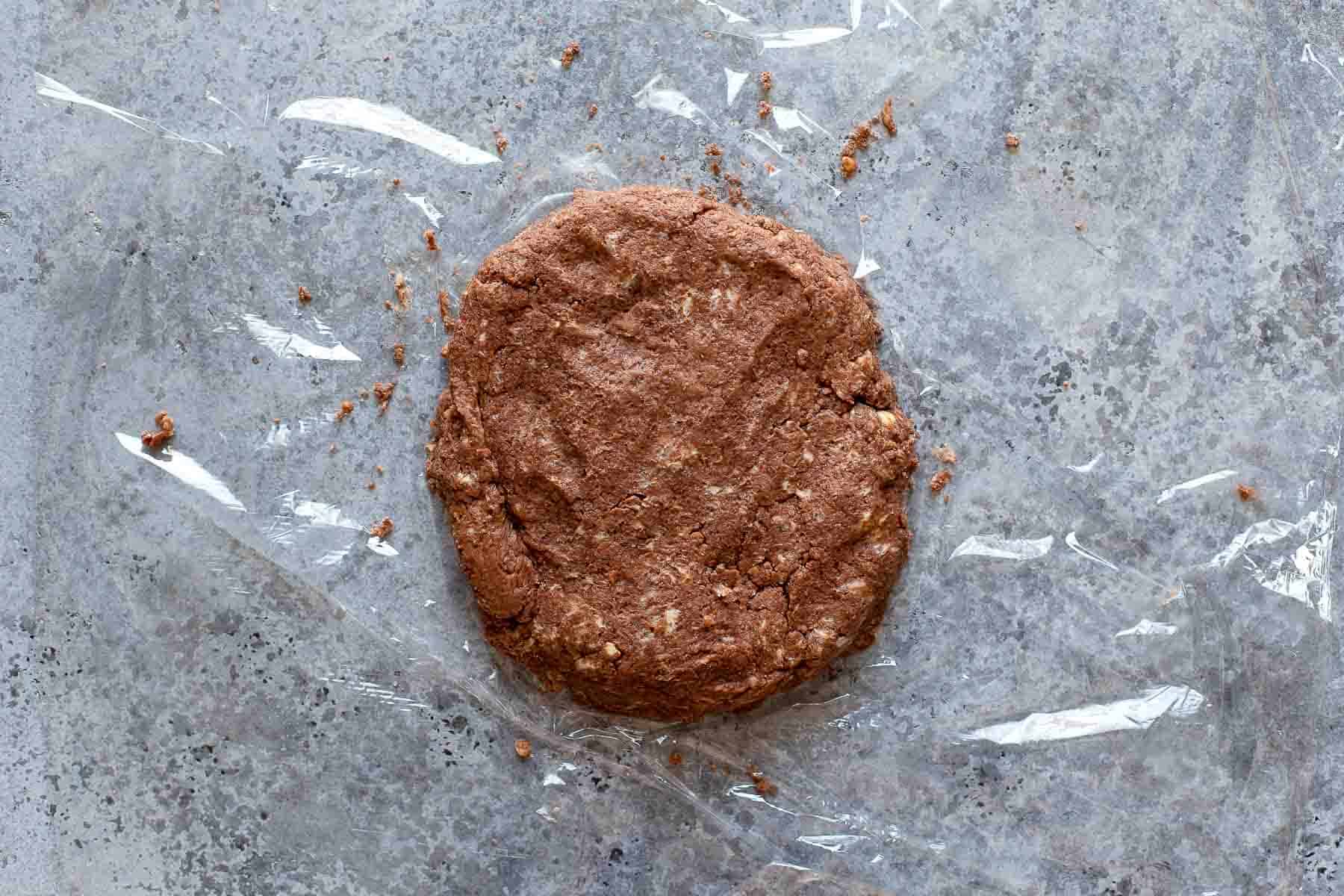 chocolate pie crust shaped into a disc sitting on a piece of plastic wrap