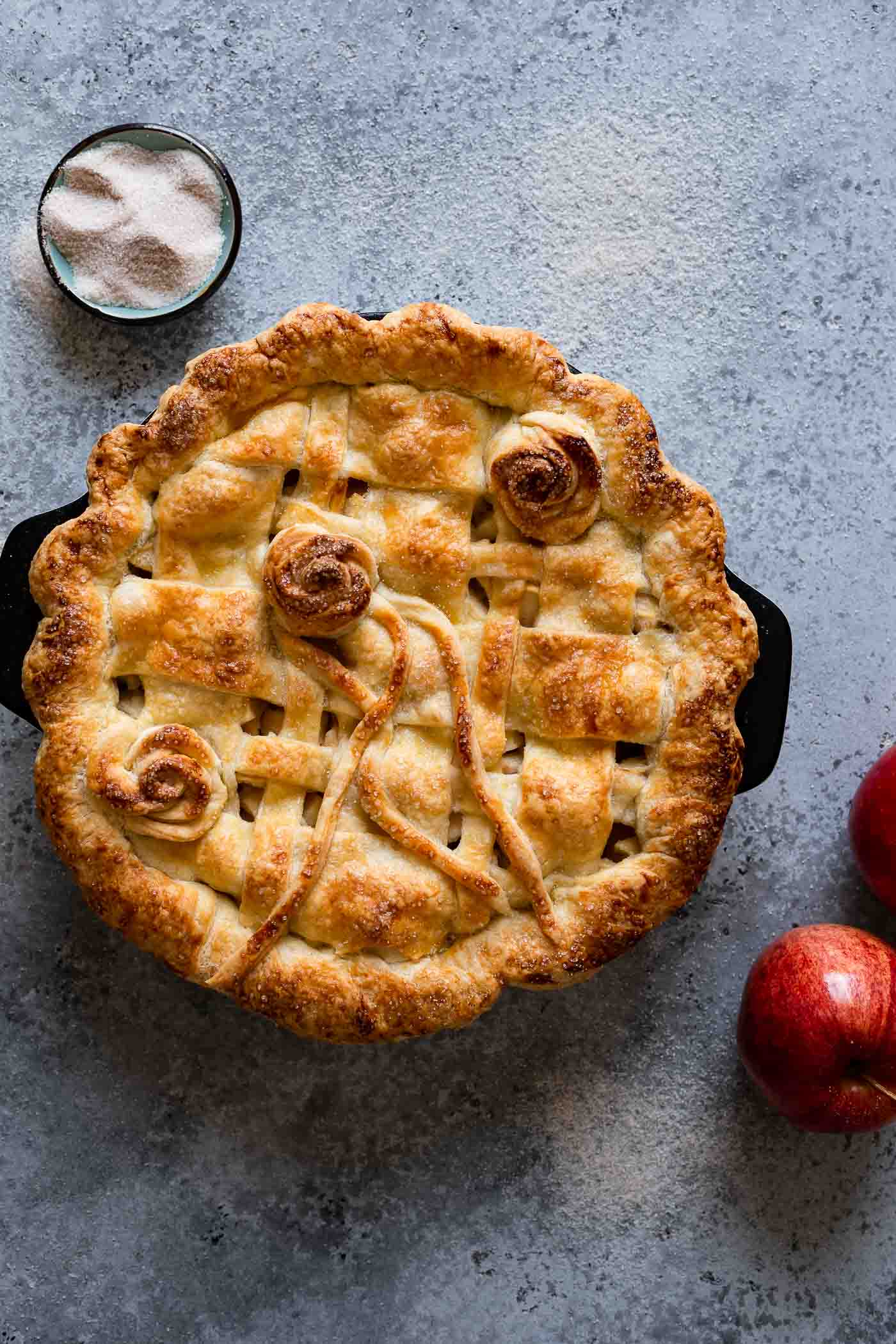 baked apple pie in a pie dish decorated with sugar and red apples