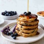 pouring syrup onto a stack of pancakes