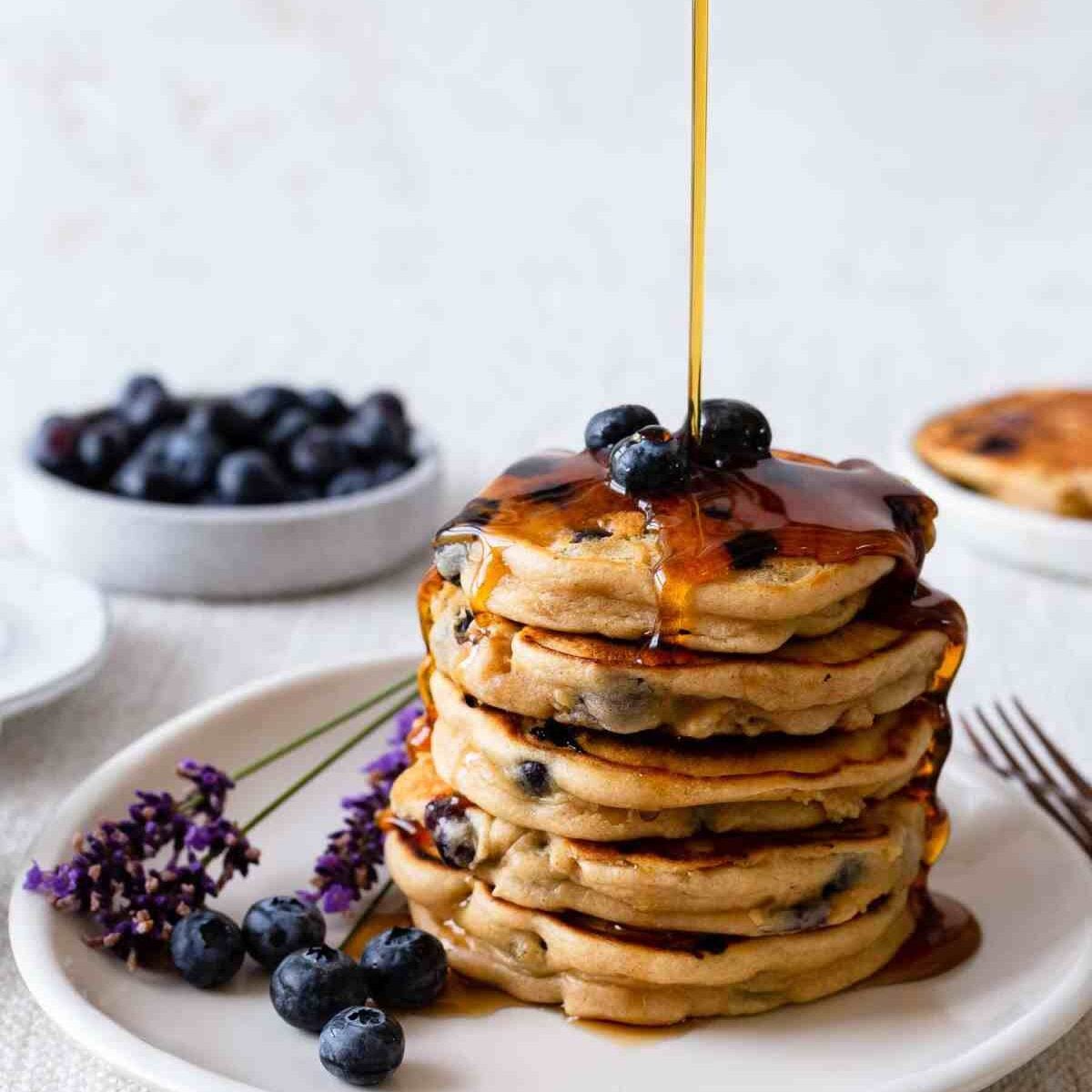 pouring syrup onto a stack of pancakes