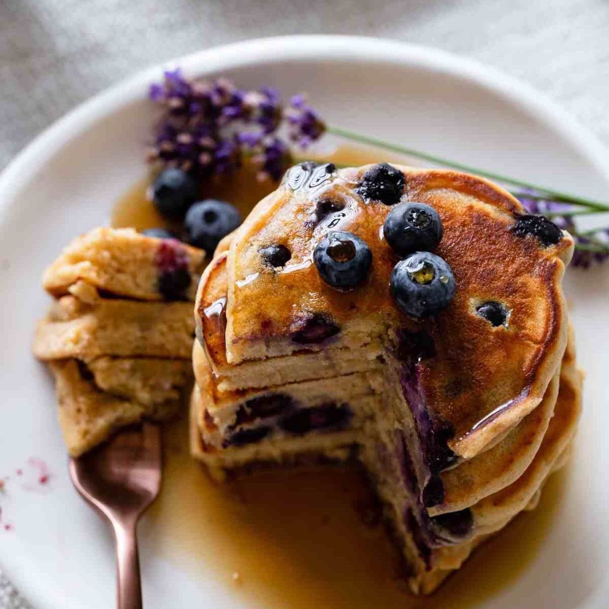 fork with a bite of pancakes and a stack of pancakes