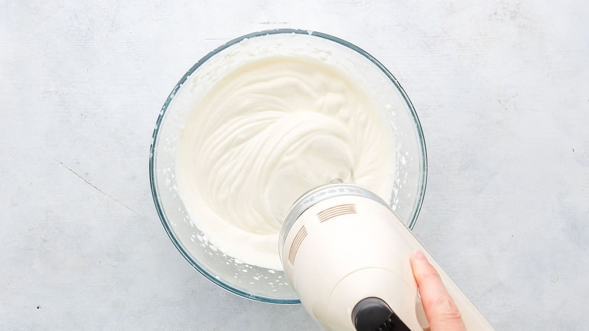 mixing heavy whipping cream in glass bowl with hand mixer on bright background
