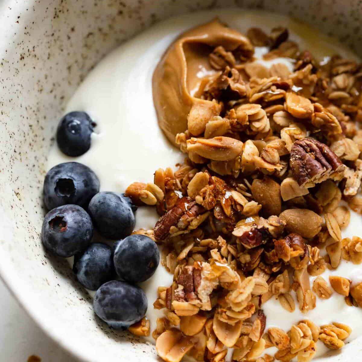 granola in a bowl with milk, peanut butter, and blueberries
