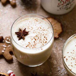 Decorative picture of eggnog in glasses with holiday decoration around on brown background