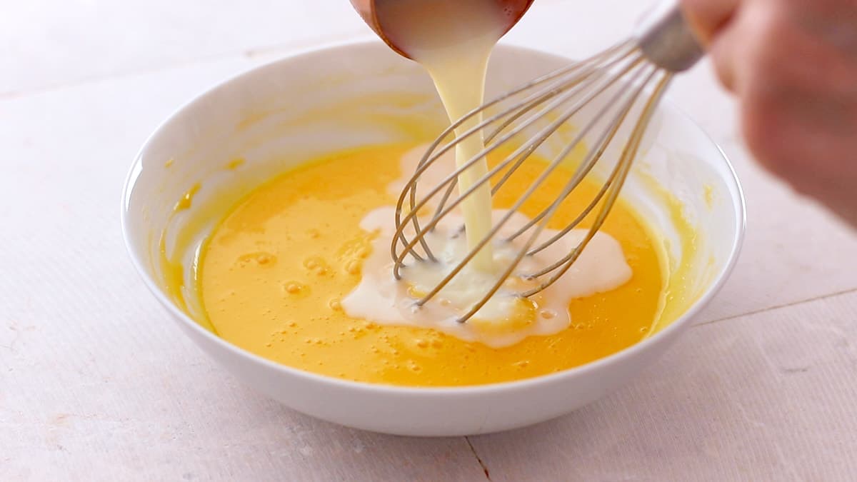 Whisking hot milk into the egg yolks mixture