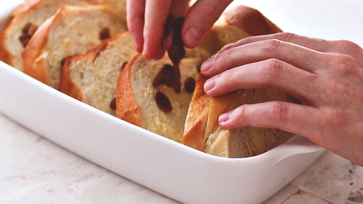 Sprinkling raisins between layers of buttered bread in baking dish