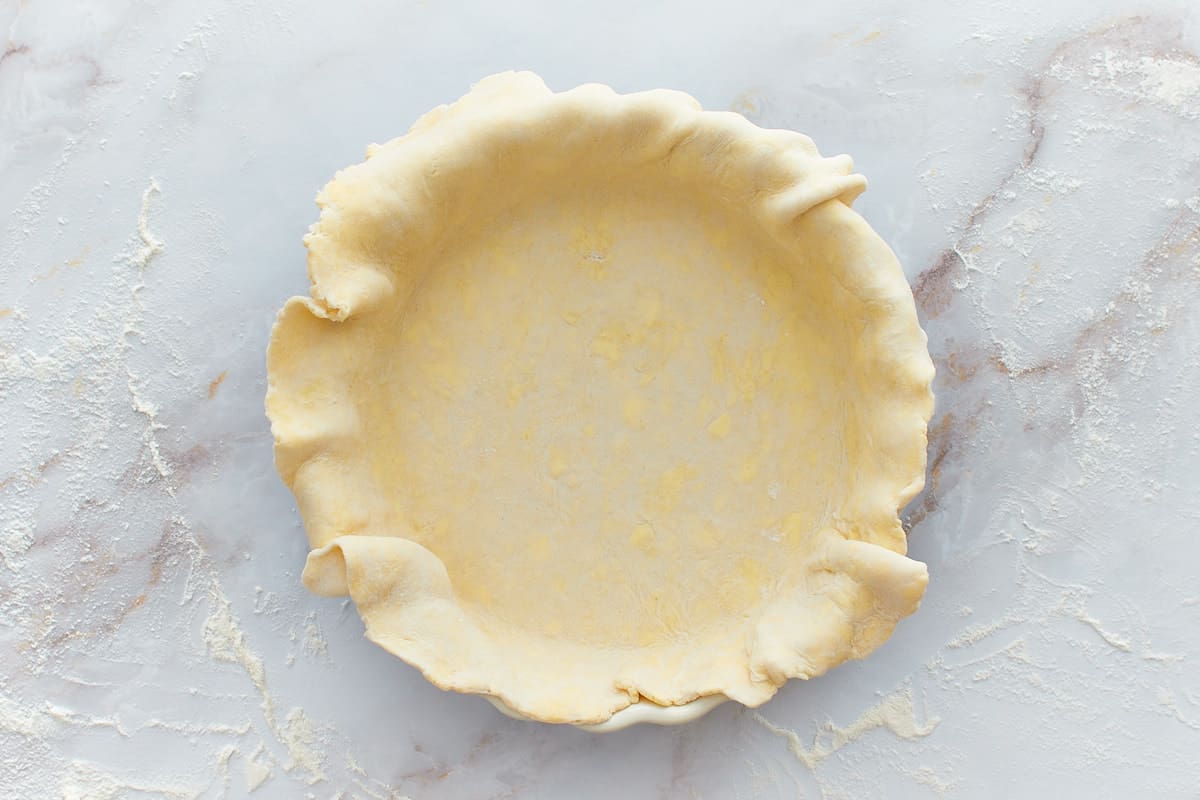 Unbaked pie crust in pie dish with dough hanging out around the sides