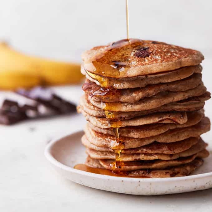 Stack of banana pancakes with syrup being poured over it