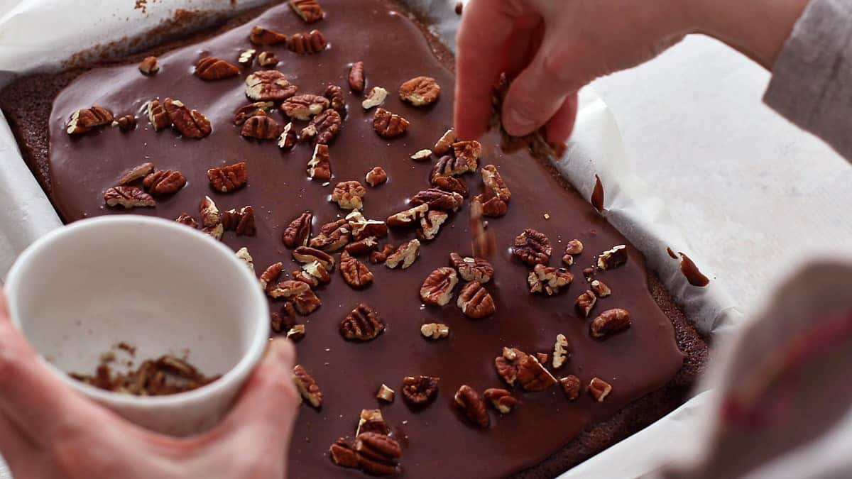 Sprinkling pecans on top of the frosted cake