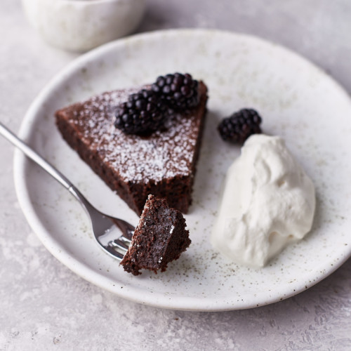 Sugar dusted cake on a dessert plate with berries on top and whipping cream