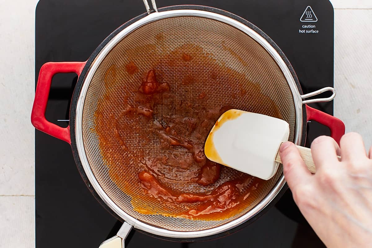 Pressing jam through a mesh strainer into a saucepan