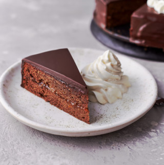 A slice of sacher torte with whipped cream on a dessert plate