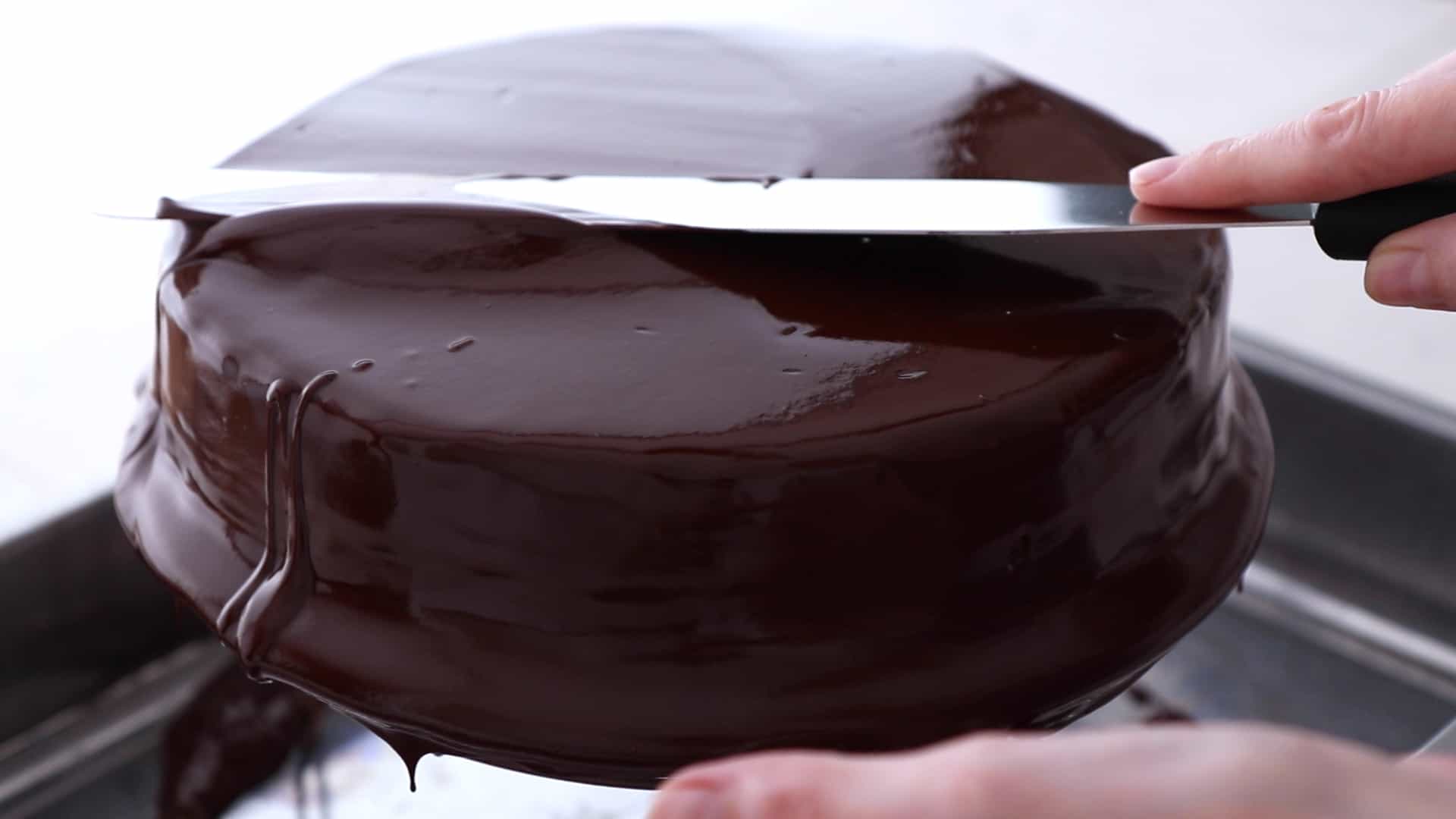 Spreading chocolate glaze over the cake with a long spatula