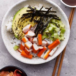 Raw ingredients and vegetables arranged on top of cooked rice in a bowl