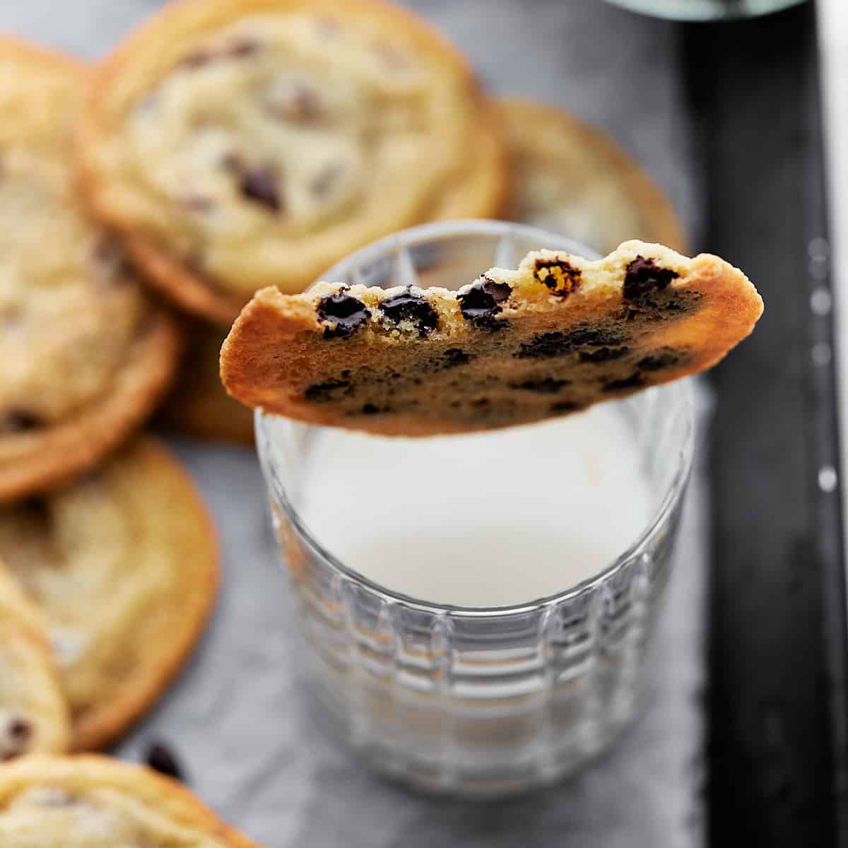 Bitten cookie placed on top of a glass of milk surrounded by other cookies