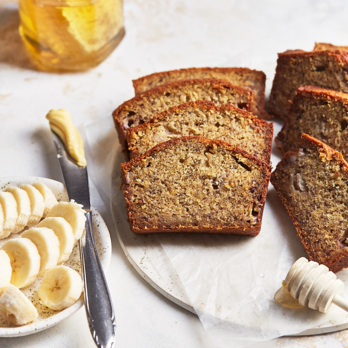 Slices of banana bread on a serving plate with butter, honey, and bananas