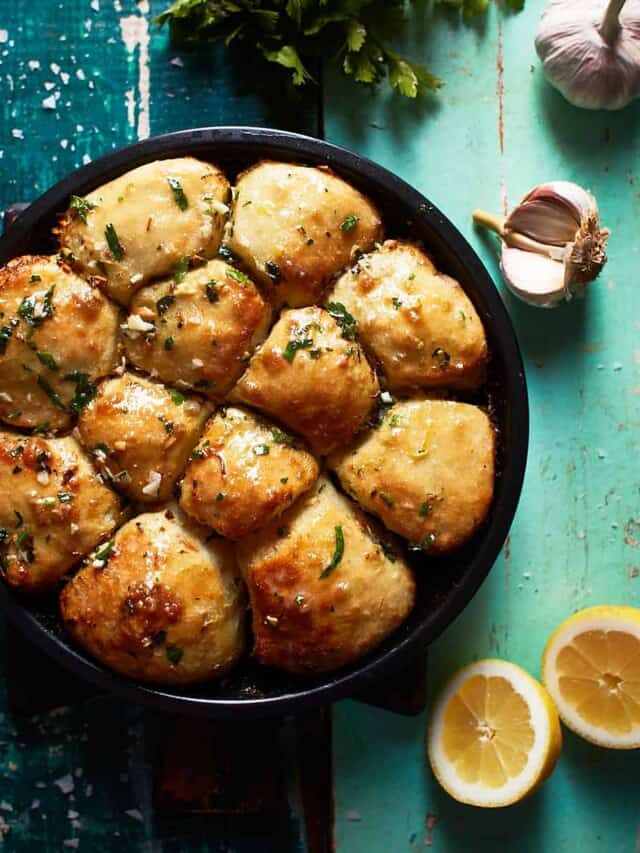 Balls of garlic bread in a baking pan with parsley, garlic, and lemon decoration