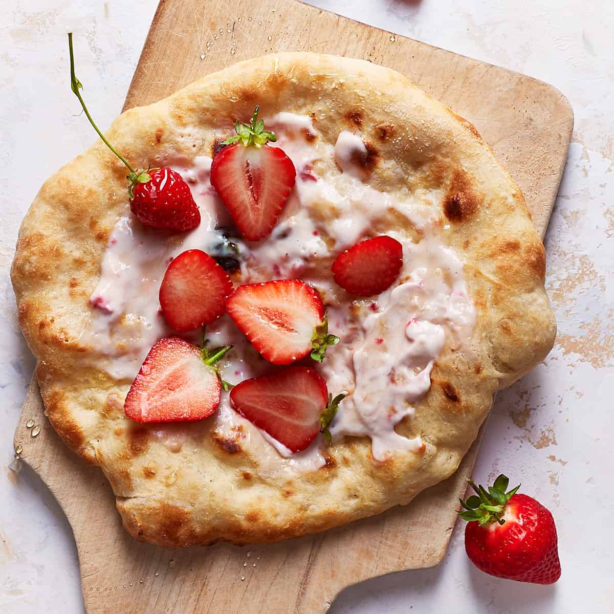 Baked strawberry pizza with fresh strawberries on top on a large wooden board
