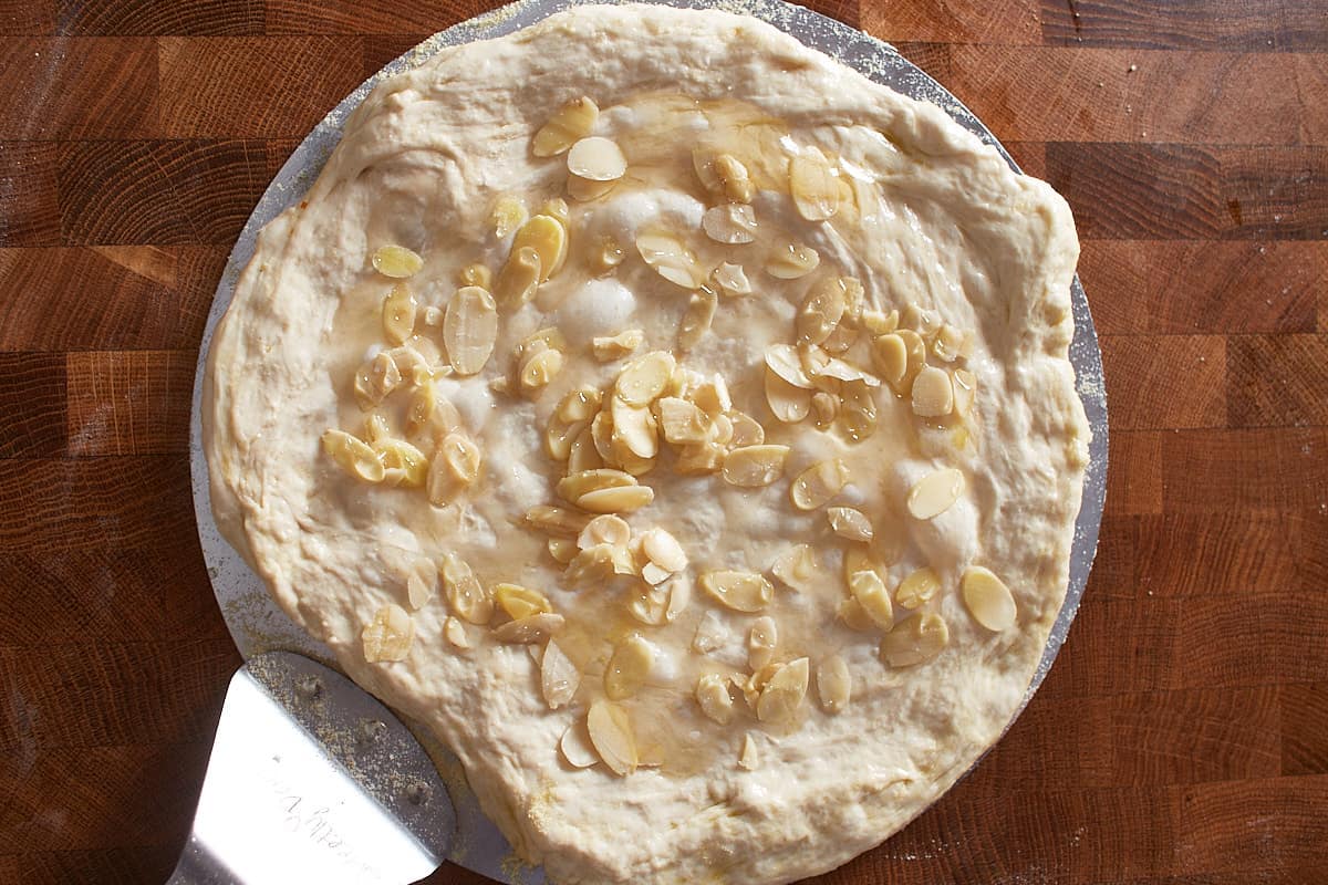 Raw dough on pizza peel topped with almond slices and honey