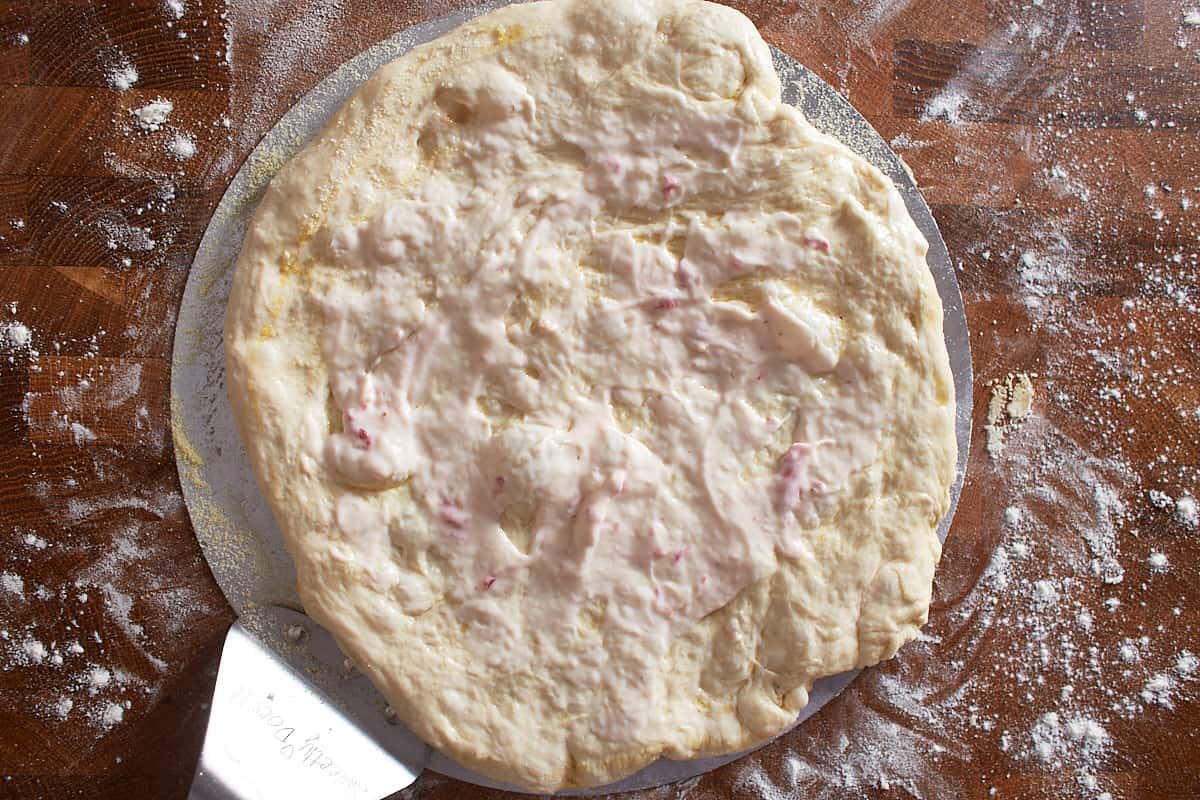 Raw dough on pizza peel spread with a strawberry and cream cheese mixture