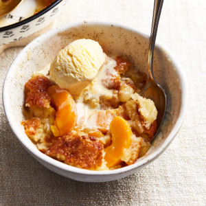 A bowl filled with soft peaches, baked topping, and melting ice cream