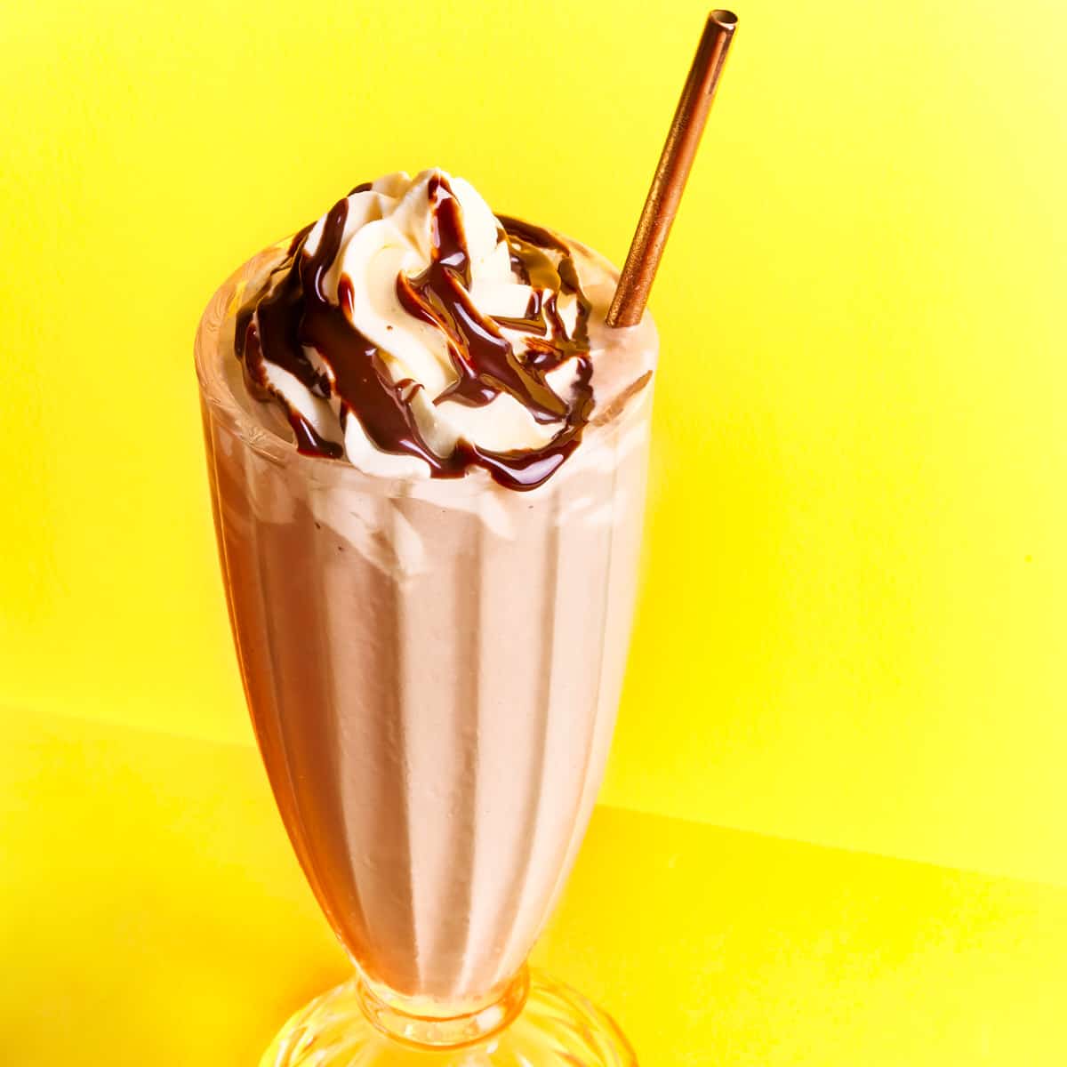 Chocolate milkshake in a glass topped with whipped cream and chocolate syrup